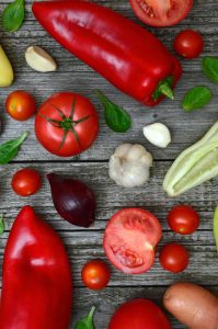 Vibrant fresh vegetables including tomatoes, peppers, and garlic on a rustic wooden surface.